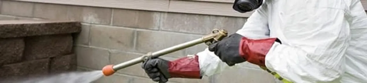 Pest control technician applying exterior insect treatment along a home foundation in Memphis, TN