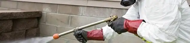 Pest control technician applying exterior insect treatment along a home foundation in Memphis, TN