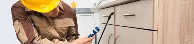 Roach exterminator applying treatment under kitchen cabinets in Memphis, TN