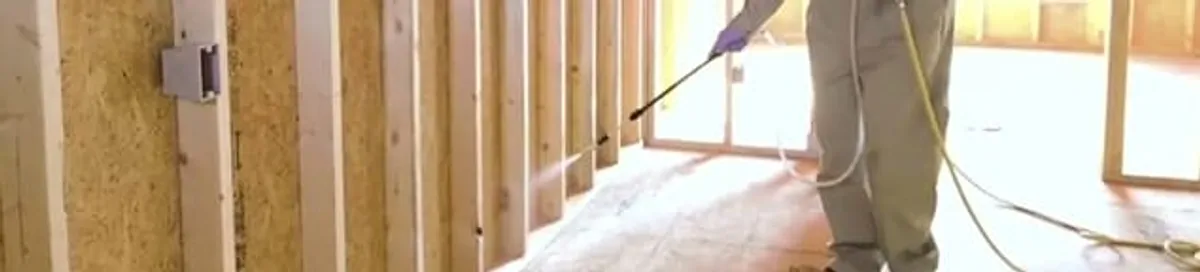 Termite treatment technician applying spray along framing and unfinished walls in Memphis, TN