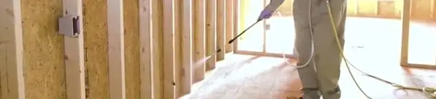 Termite treatment technician applying spray along framing and unfinished walls in Memphis, TN